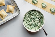 a bowl of spinach dip next to some crackers on a baking sheet and a cookie sheet