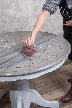 a person with a brush on top of a round table that has been painted white