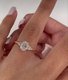 a woman's hand holding an engagement ring with a diamond on it and the other hand