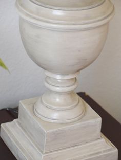 a white urn sitting on top of a wooden table next to a flower pot