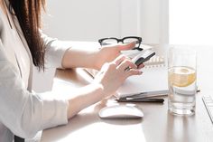 a woman sitting at a table with a laptop and cell phone in her hand while looking at the screen