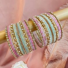 several different colored bracelets on a wooden stick with pink and white feathers in the background