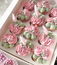 pink and green cupcakes in a box with pearls on the top are decorated with feathers