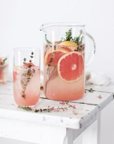 a pitcher filled with pink lemonade and garnish next to two glasses full of water