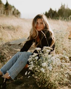 a beautiful young woman sitting on top of a grass covered field next to wildflowers