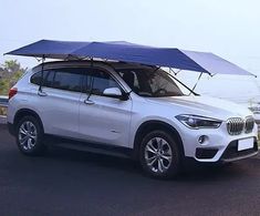 a white bmw suv parked on the side of the road with an umbrella over it's roof