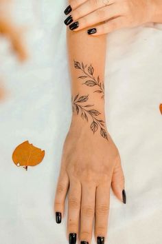 a woman's hand with black nail polish and leaf tattoos on her left arm