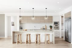 an open kitchen with three stools in front of the island and two lights hanging from the ceiling