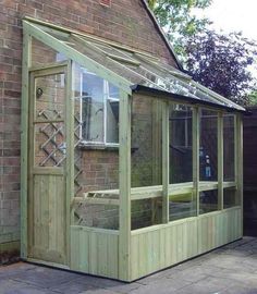 a wooden greenhouse with glass doors and windows on the side of a brick building next to a tree