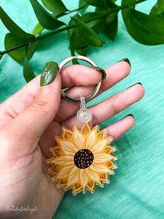 a hand holding a yellow and black flower shaped keychain on top of a green table