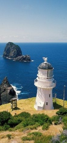 a white lighthouse sitting on top of a lush green hillside next to the ocean with an island in the background