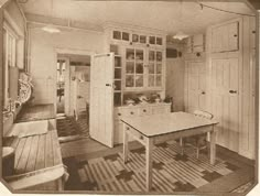 an old black and white photo of a dining room with table, cupboards and chairs