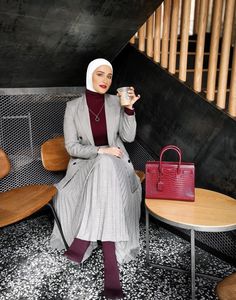 a woman sitting on a bench holding a cup in her hand and wearing a hijab