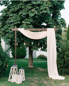 an outdoor wedding ceremony with white draping and lanterns hanging from the trees, surrounded by lush greenery