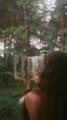 a woman is reading a book in the woods