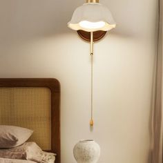 a white vase sitting on top of a bed next to a wall mounted light fixture