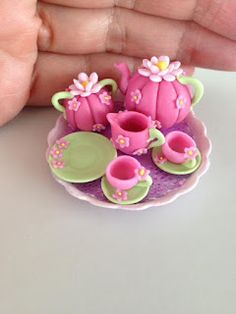 a hand is holding a small pink flower pot and tea set on a saucer