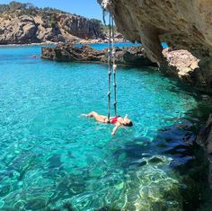 a person hanging from a rope in the water near some cliffs and blue water with rocks