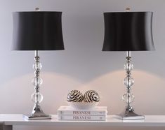 two lamps sitting on top of a white table next to books and a lamp shade