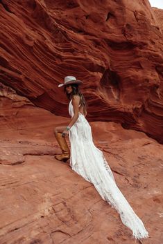 a woman in a white dress and cowboy hat sitting on the ground near some rocks