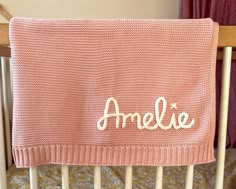 a pink blanket with the word amelie written on it in white lettering, sitting on top of a crib