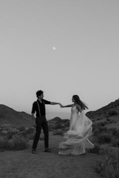 a man and woman dancing in the desert at sunset with moon behind them, black and white photograph