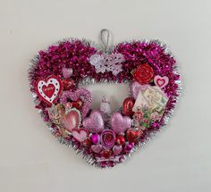 a heart shaped wreath with pink and red decorations hanging on the wall next to a white wall