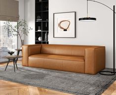 a brown leather couch sitting on top of a wooden floor next to a table and lamp