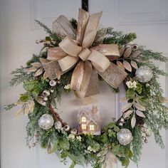 a christmas wreath hanging on the front door with a lit house in the center and greenery around it