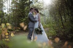 a bride and groom standing in the woods