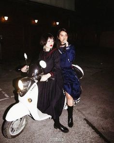 two women sitting on the back of a scooter