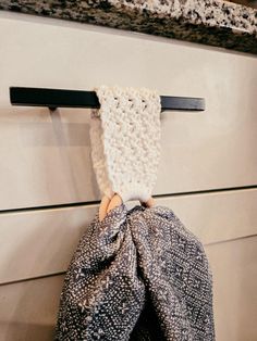 a hand is holding a knitted item in front of a kitchen cabinet door handle