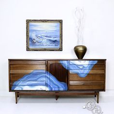 a painting is hanging on the wall next to a wooden dresser with blue and white designs