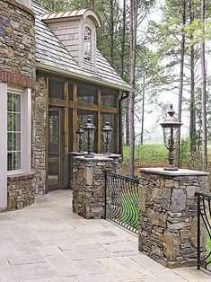 a stone house with an iron gate and lantern lights on the front porch, surrounded by trees