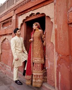 a man standing next to a woman in a red and gold wedding dress on the side of a building