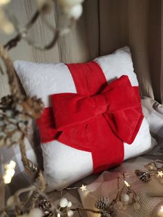 a white pillow with a red bow on it sitting next to christmas decorations and lights