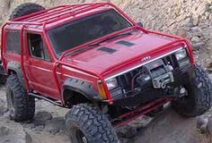 a red four - doored truck driving on rocks