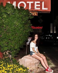 a woman sitting on top of a rock in front of a sign that says motel