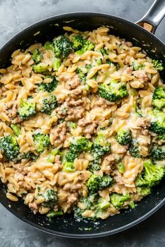 a skillet filled with pasta and broccoli on top of a gray counter