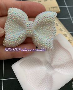 a hand holding a small white bow with sequins on it