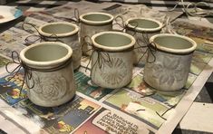 six ceramic jars with designs on them sitting on top of a table covered in newspaper