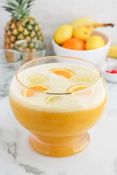 an orange drink in a glass on a marble table with fruit and bowls behind it