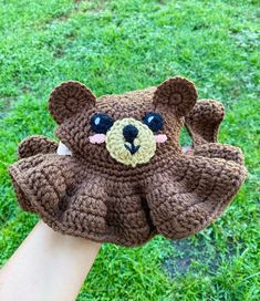 a hand holding a brown crocheted teddy bear on it's thumb with grass in the background