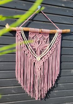 a pink macrame hanging on the side of a building with beads and wood