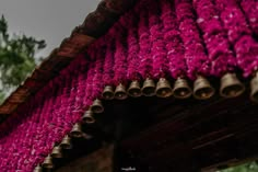 bells hanging from the roof of a building with purple flowers on it's side