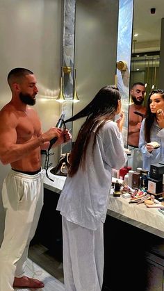 a man and woman standing in front of a bathroom mirror while brushing their long hair