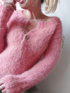 a woman wearing a pink sweater with buttons on the front and back, leaning against a white wall