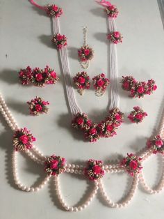 an assortment of necklaces and bracelets with pink flowers on white pearls are displayed