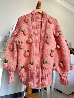 a pink knitted sweater with roses on the front and back, hanging from a wooden chair