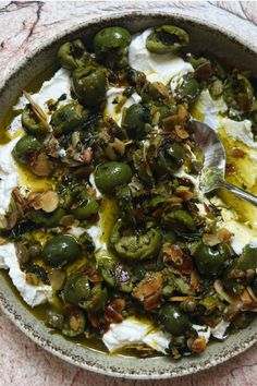 a bowl filled with sour cream and green peppers on top of a table next to a spoon